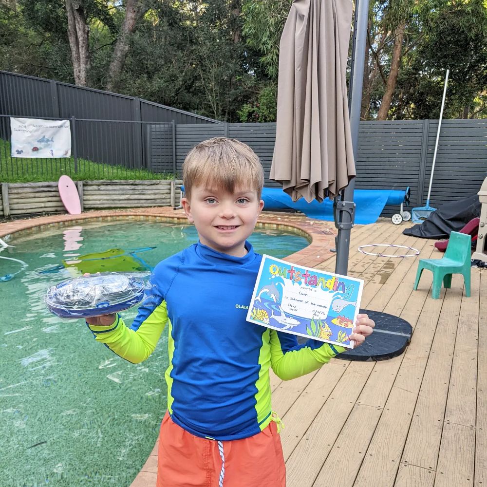 Young swimmer proudly holding his end-of-season certificate