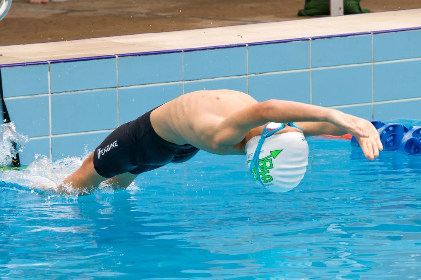 Swimmer in an ACM Swimming cap stretching out into freestyle